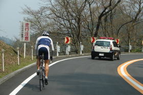 前後を警察車両に護られてテスト走行をする松丸真幸選手(全日本トライアスロン王者)